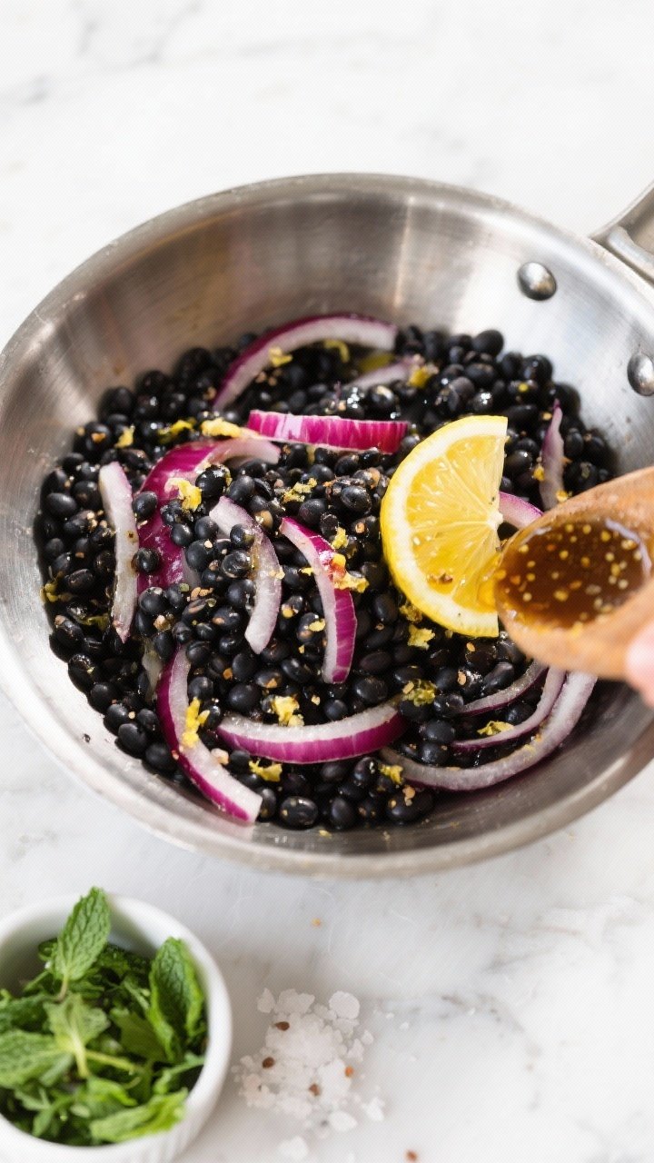 Cooking process: Warm black beluga lentils being tossed with thinly sliced red onion and half the le